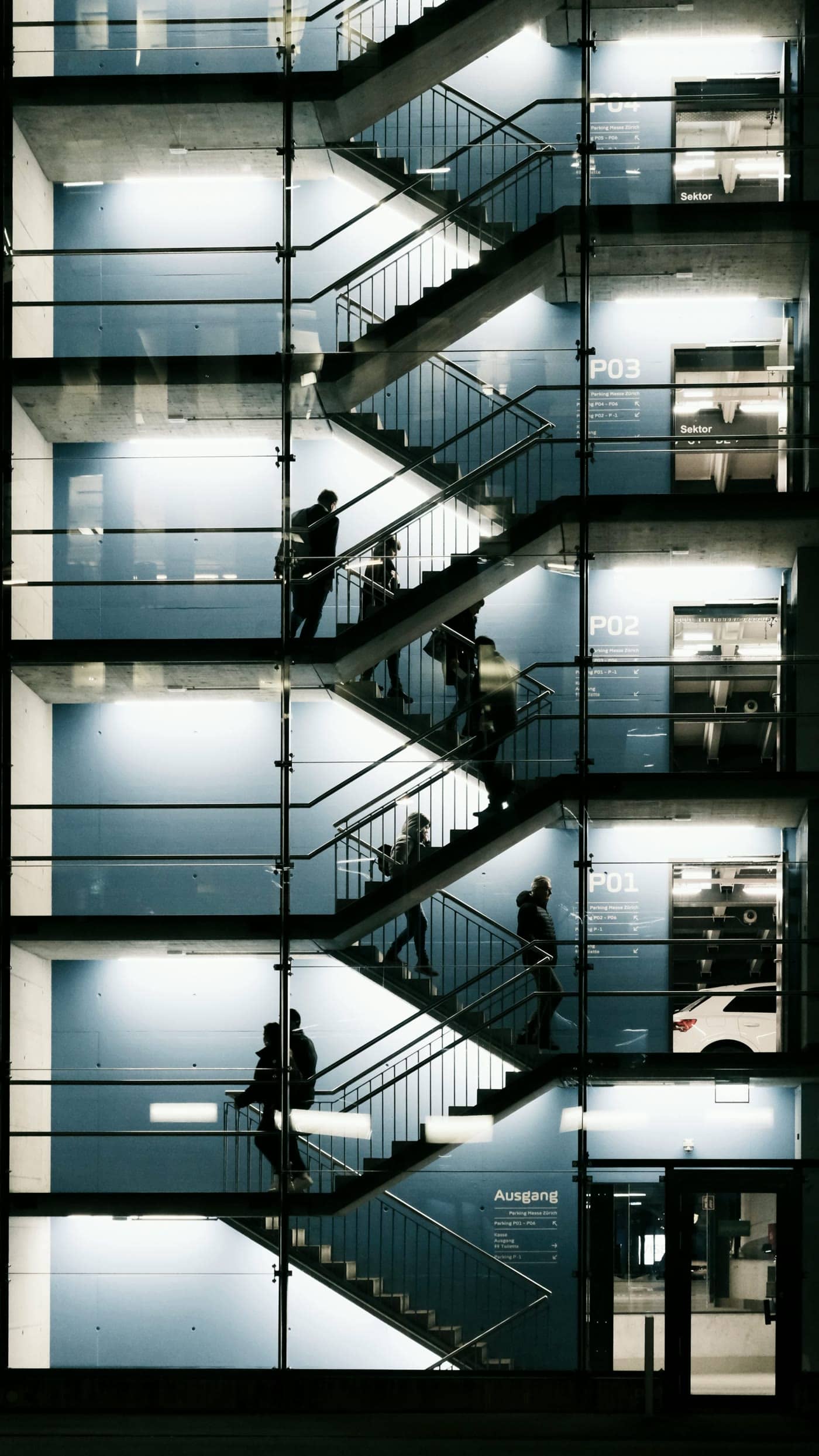 Personas subiendo por la escalera acristalada e iluminada de un edificio de oficinas de noche