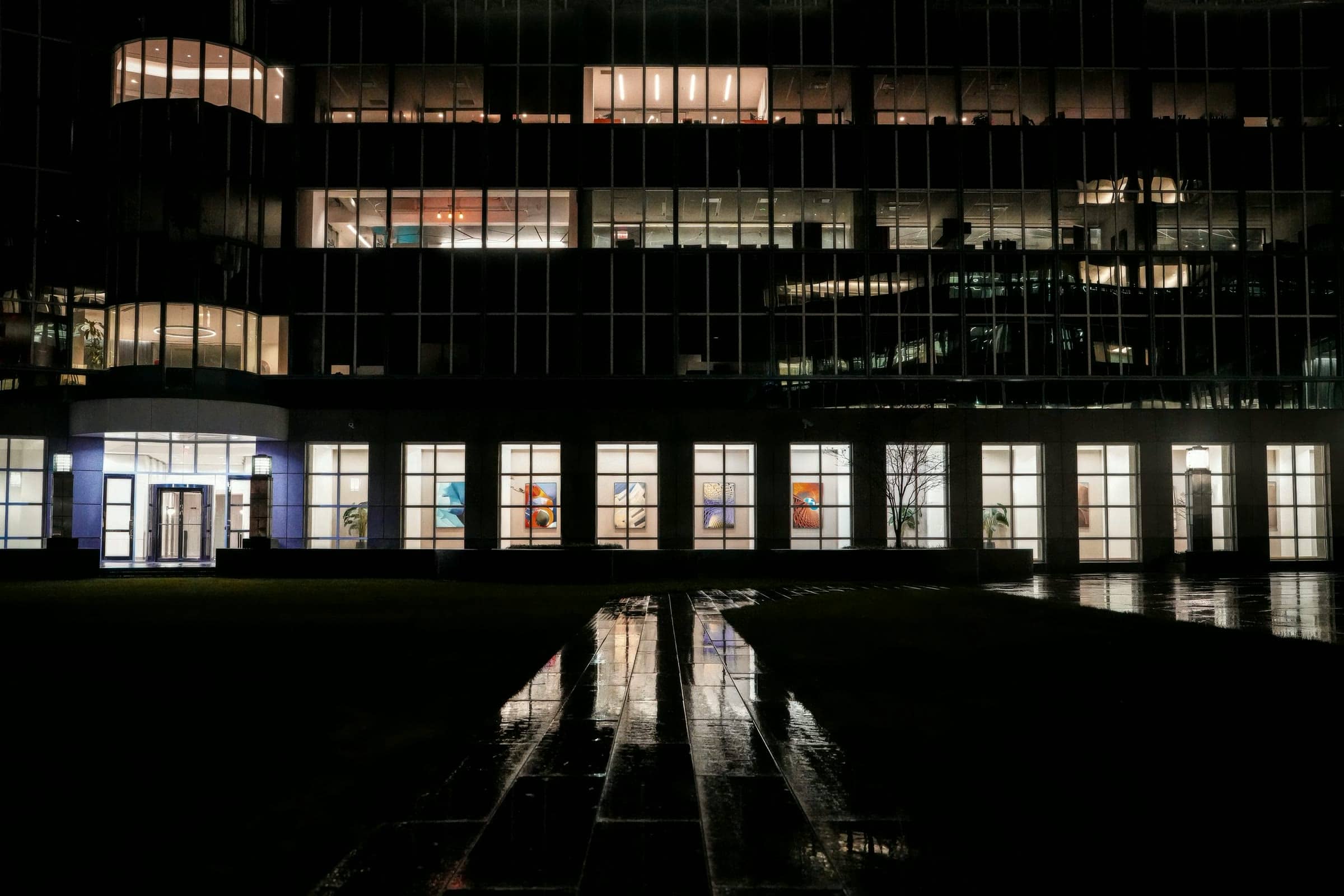 Edificio de oficinas iluminado de noche reflejado en el pavimento mojado